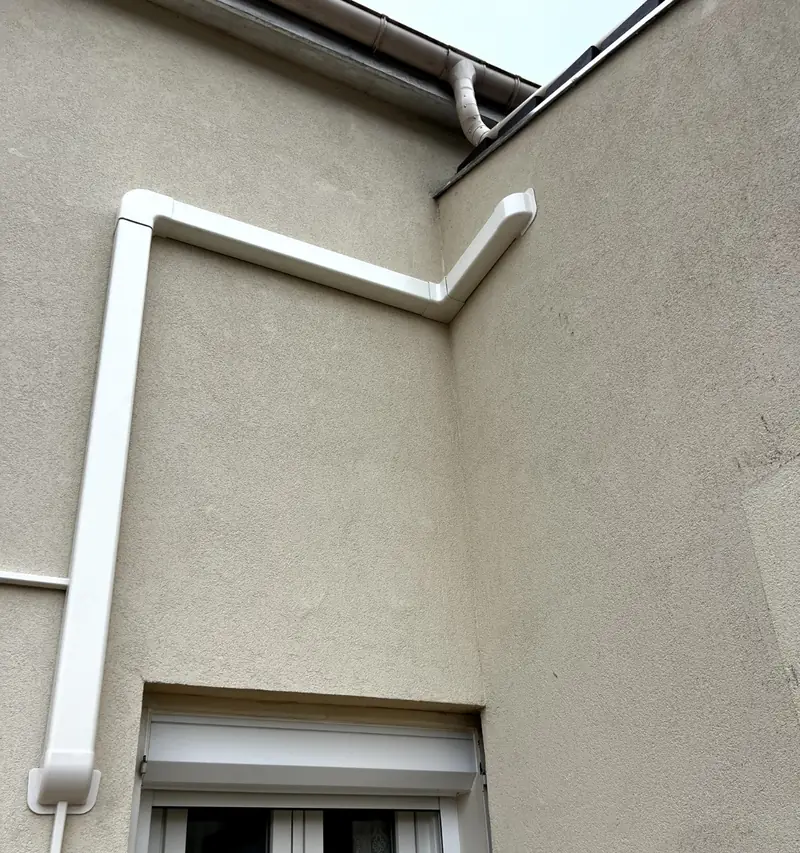 Goulotte blanche descendant le long d'une façade enduite jusqu'au passage de mur
