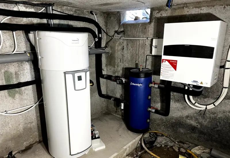Local technique en sous-sol : module intérieur de pompe à chaleur, ballon tampon bleu et ballon d'eau chaude