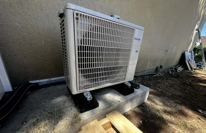 Unité extérieure de pompe à chaleur posée sur une dalle béton neuve, supports anti-vibratiles