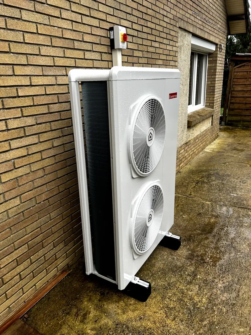 Unité extérieure de pompe à chaleur air/eau à deux ventilateurs posée contre un mur de briques
