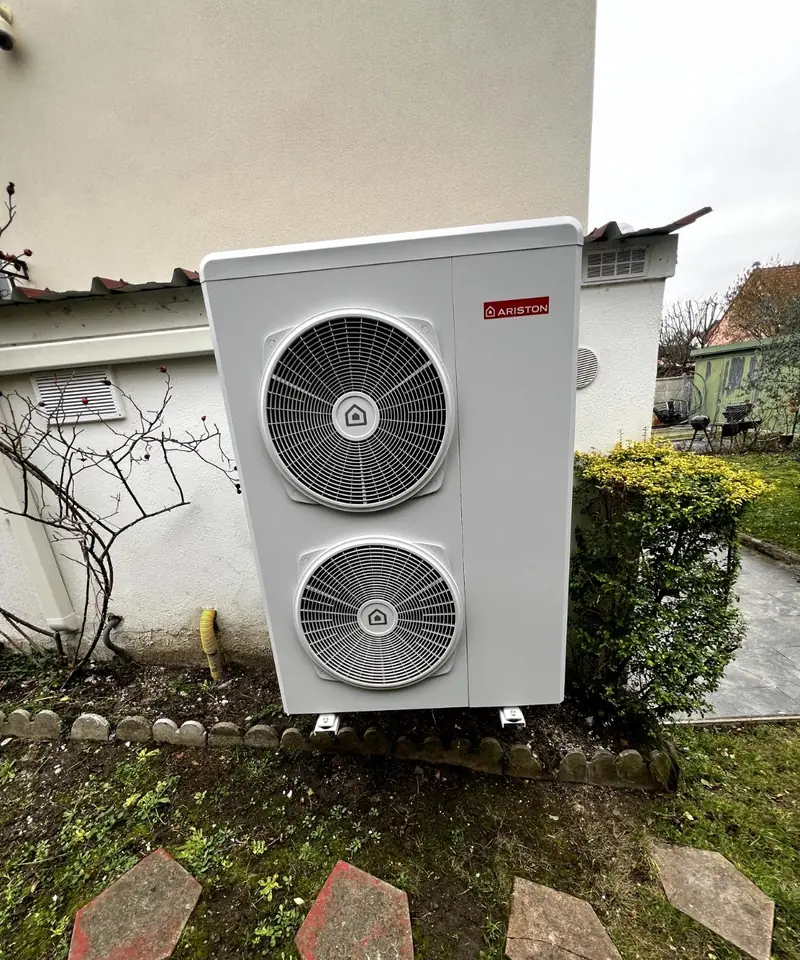 Unité extérieure de pompe à chaleur air/eau installée au pied d'une maison, côté jardin