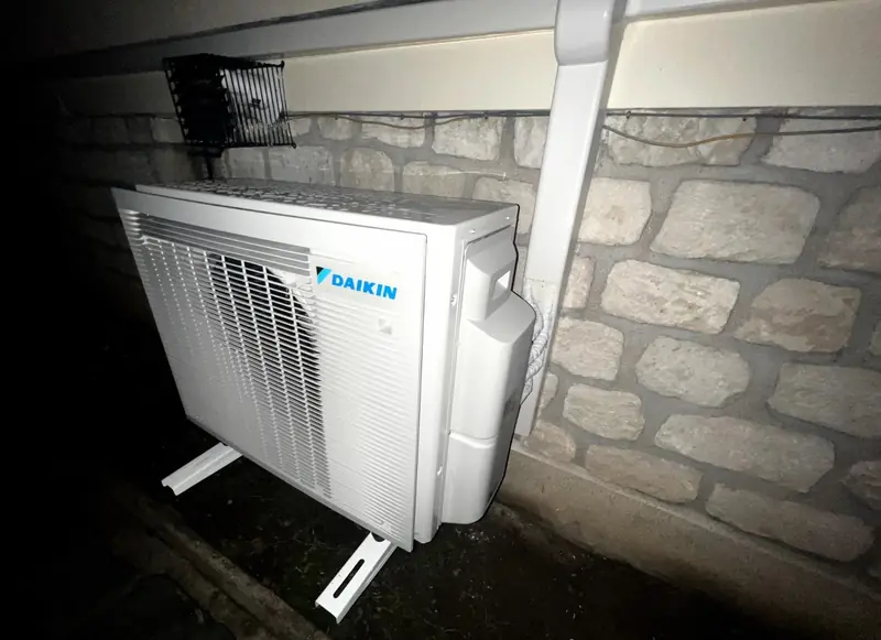 Unité extérieure de pompe à chaleur air/air fixée sur supports contre un mur en pierre